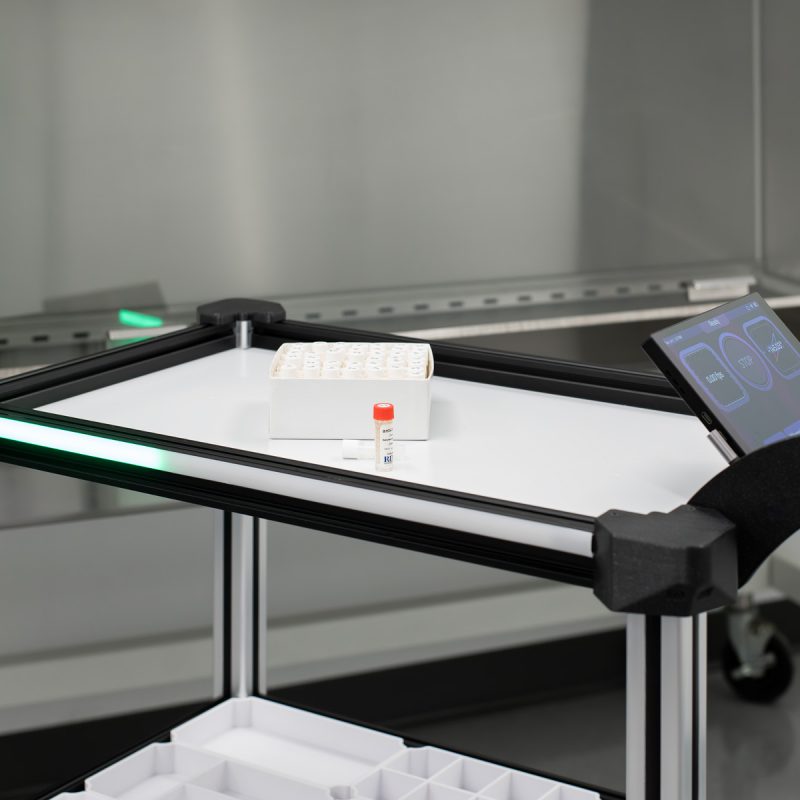 Model C2 Autonomous Robot Cart pictures in a laboratory research environment, in front of a freezer, with a box of sample vials on its top shelf.