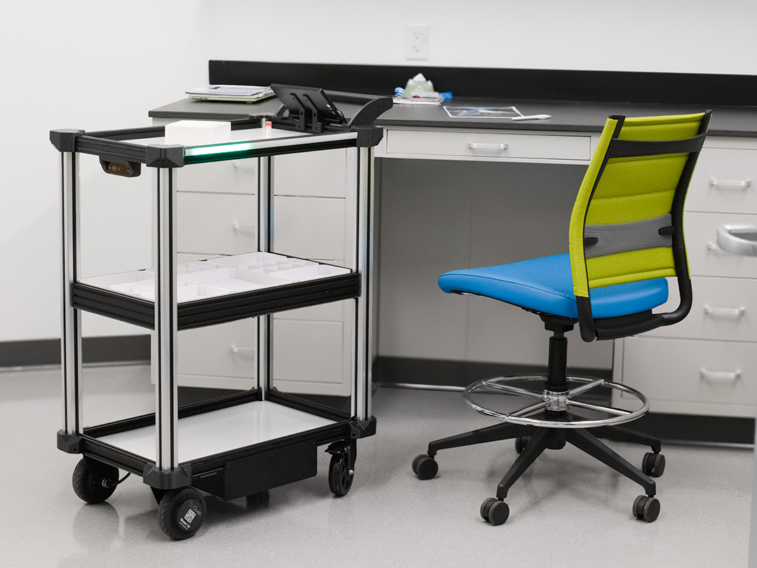 Model C2 autonomous mobile robot standing near a doctors examination desk next to a counter table and chair.