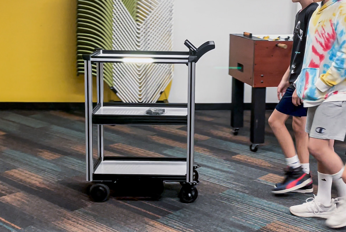 Model C2 robotic cart seen leading a group of school children through a hallway on the way towards deliveries.